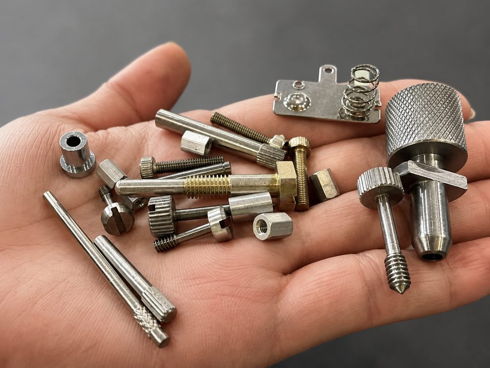 Swiss turned precision parts samples including threaded shafts, knurled knobs, spring contacts, and stepped pins manufactured by VOLCRIX